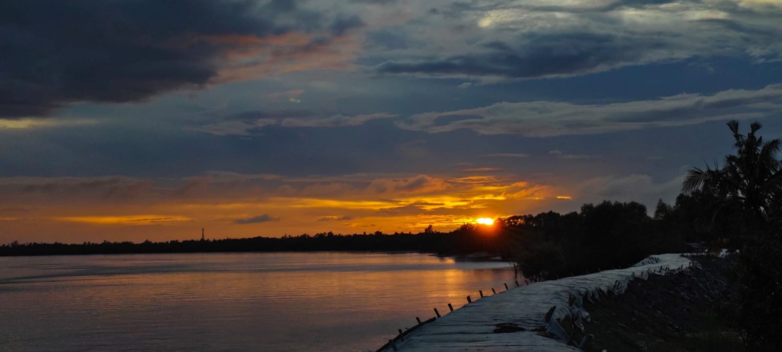 Golden sunset over a wide Sundarban river with the embankment in the foreground